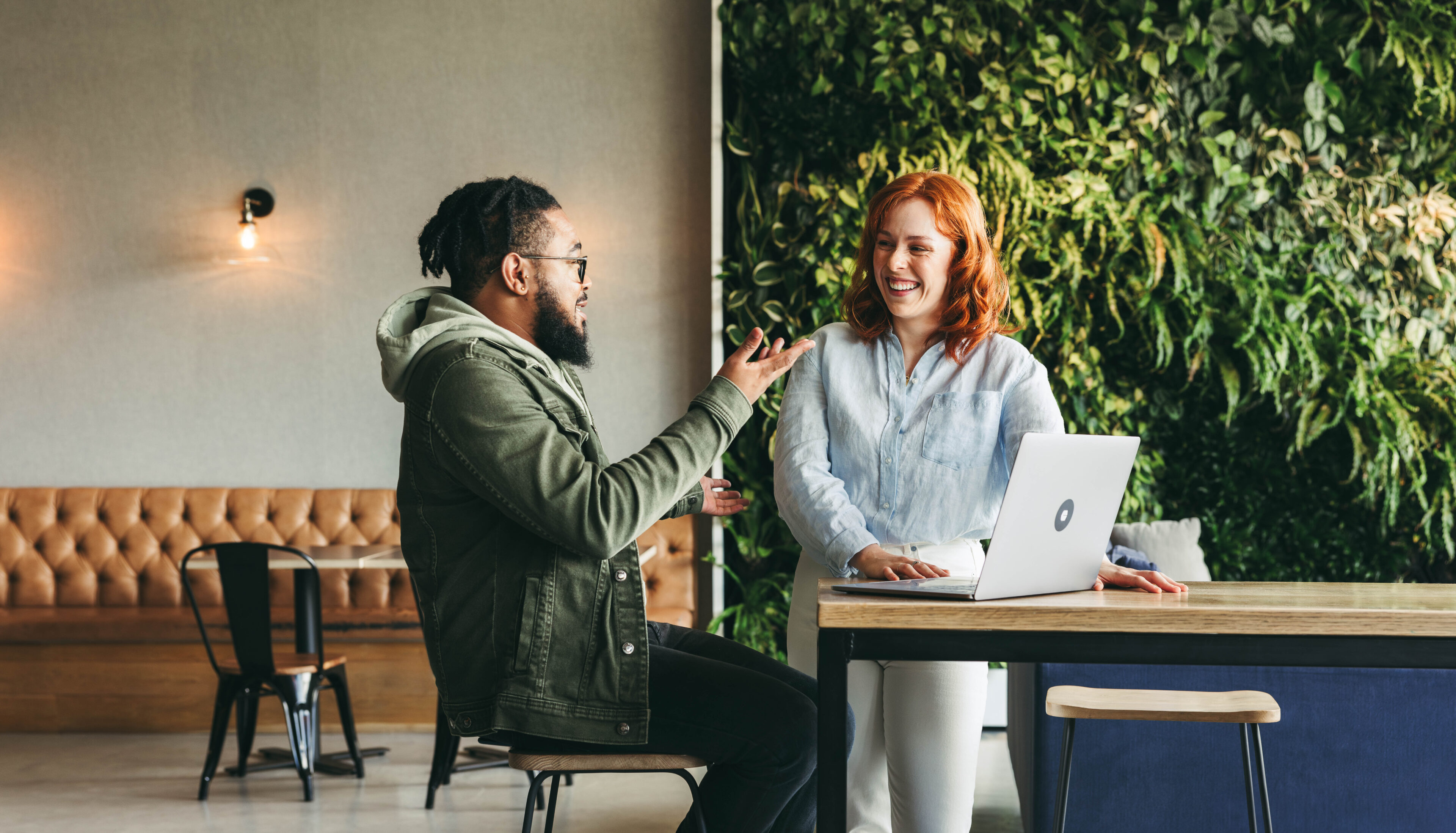 Happy coworkers collaborate in a vibrant cafe. Discussing, smiling, and working together using laptops, they create a positive and productive office environment. Professional women in the tech industry exemplify successful teamwork and remote work in a lively coworking space.